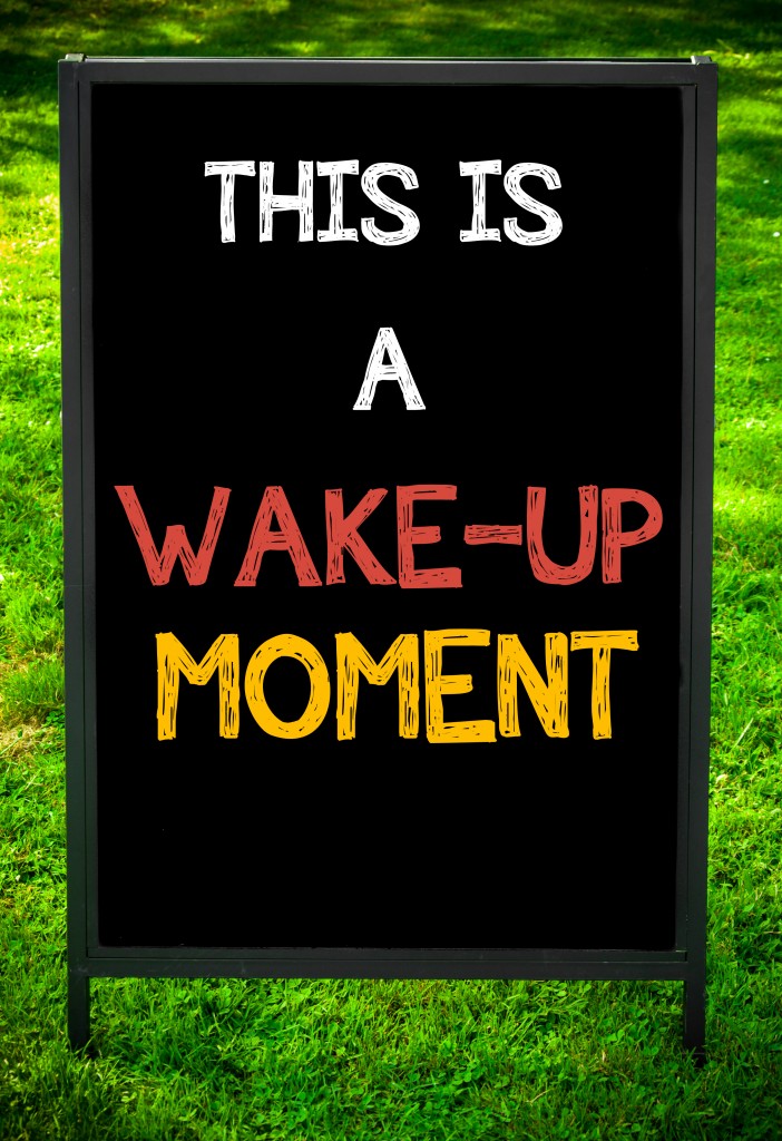 THIS IS A WAKE-UP MOMENT message on sidewalk blackboard sign against green grass background. Copy Space available. Concept image